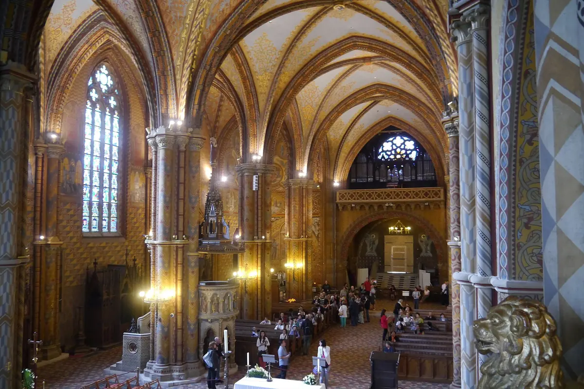 The nave of Matthias Church with slender columns, ribbed vaults and walls painted in gold, red and green patterns